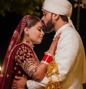 Bride and groom posing in maroon wedding outfits indoors