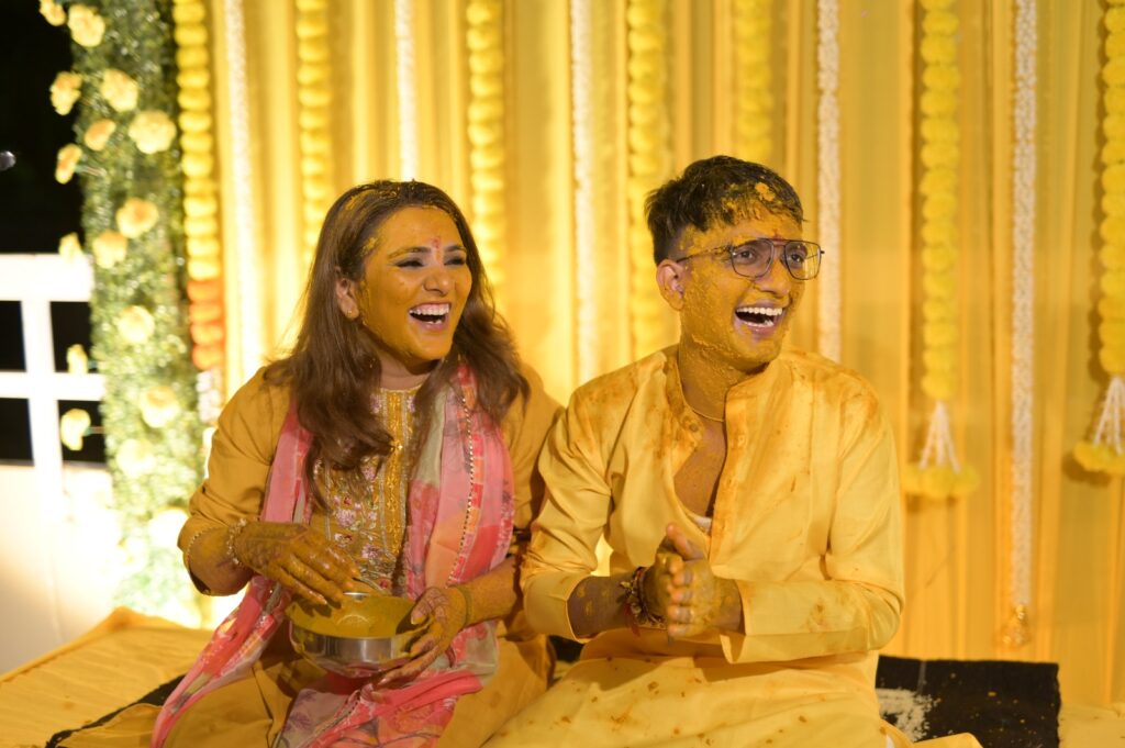 a man and woman sitting on a bed with yellow paint on their faces- couple haldi photoshoot
