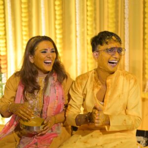 a man and woman sitting on a bed with yellow paint on their faces- couple haldi photoshoot